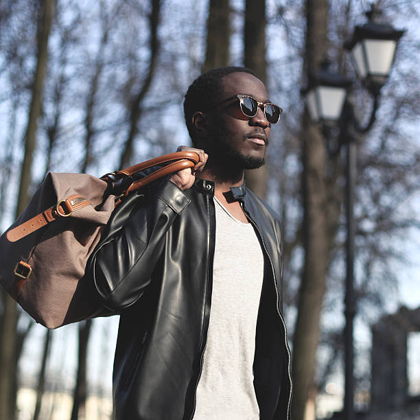 Fashion portrait of handsome african man in black leather jacket with bag outdoors